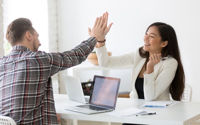 Young asian and caucasian partners giving high five at workplace, diverse motivated colleagues celebrate goal achievement, business win, successful teamwork, good result, support and victory concept